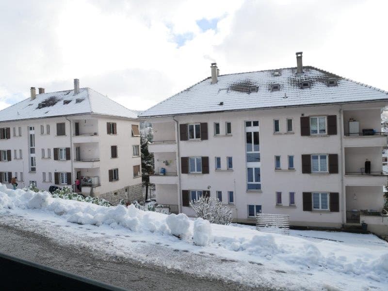 Multi-story apartment building with white exterior, snow-covered roofs, and balconies visible.