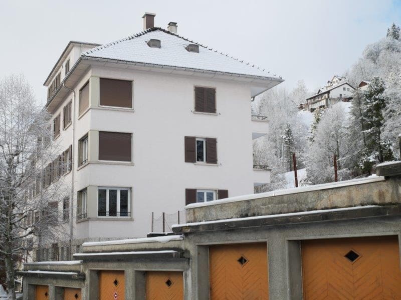 3-story white apartment building with brown shutters, garage doors, and a snowy roof