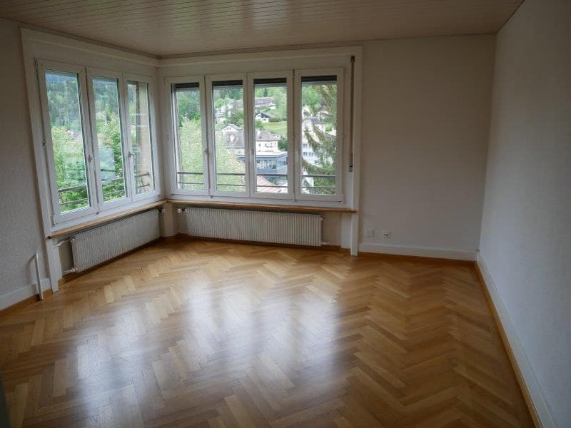 Spacious living room with large windows offering a scenic view, hardwood herringbone flooring, and white walls