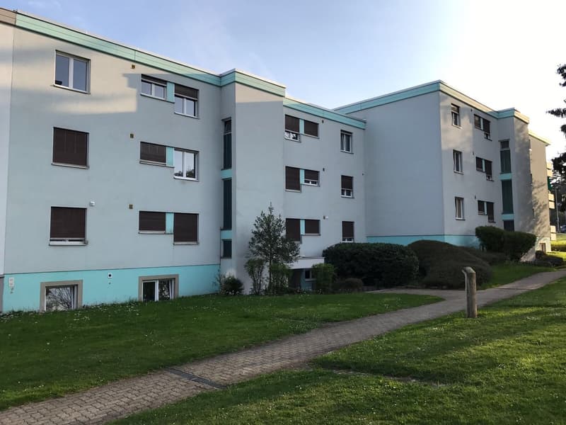 Three story apartment building, multiple windows, blue base, well-kept green lawn