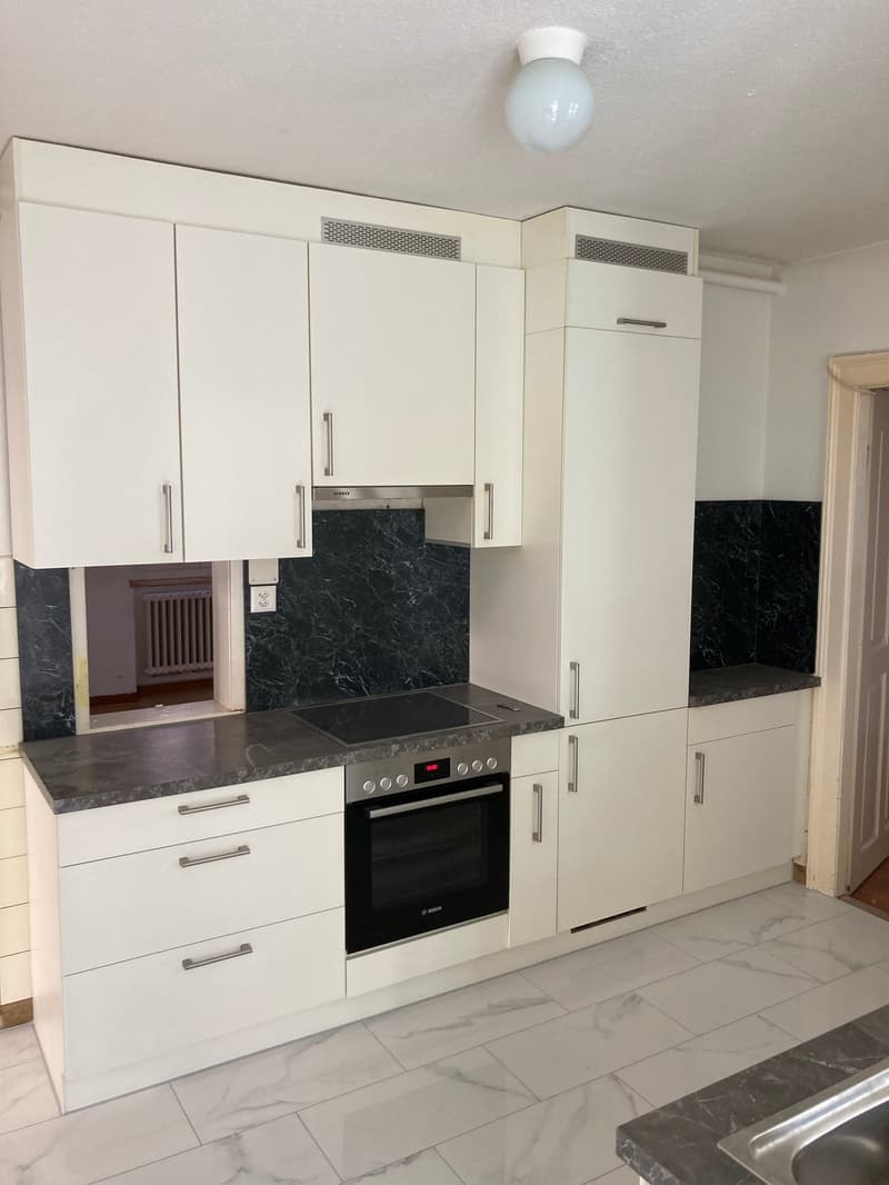 Modern kitchen with white cabinets, black marble countertops, built-in oven, and dishwasher