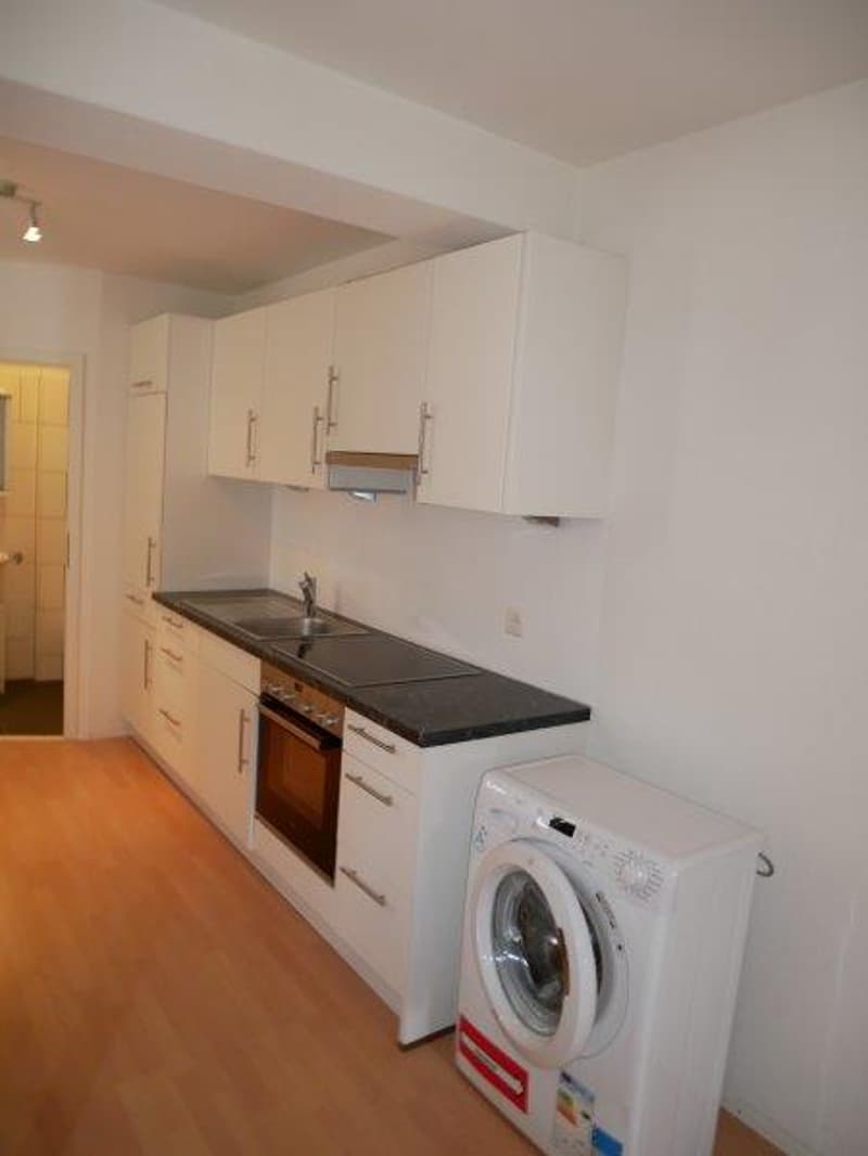 White kitchen cabinets, black countertop, built-in oven, washing machine, dishwasher