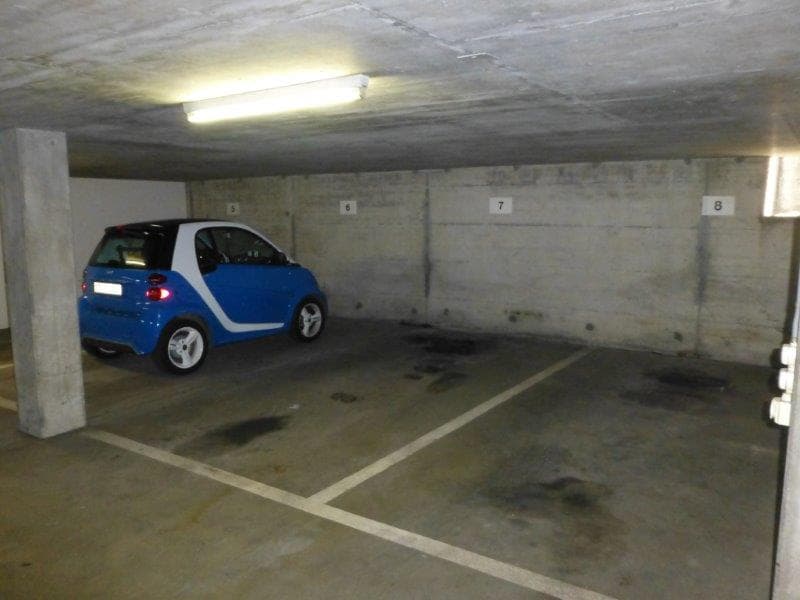Underground parking space with a blue car, white markings, concrete walls, and a ceiling light