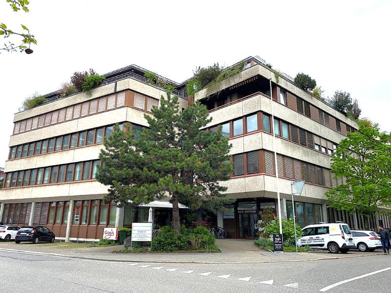 Multi-story office building with multiple windows, brown exterior, trees in front, and a roof garden.