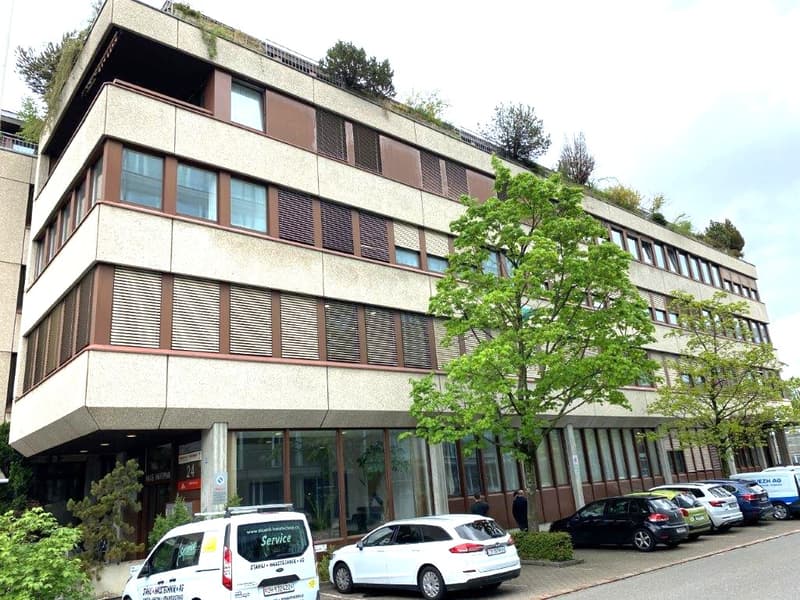 Office building, beige exterior, glass windows, 4 stories, green plant life on rooftop, street view, cars parked