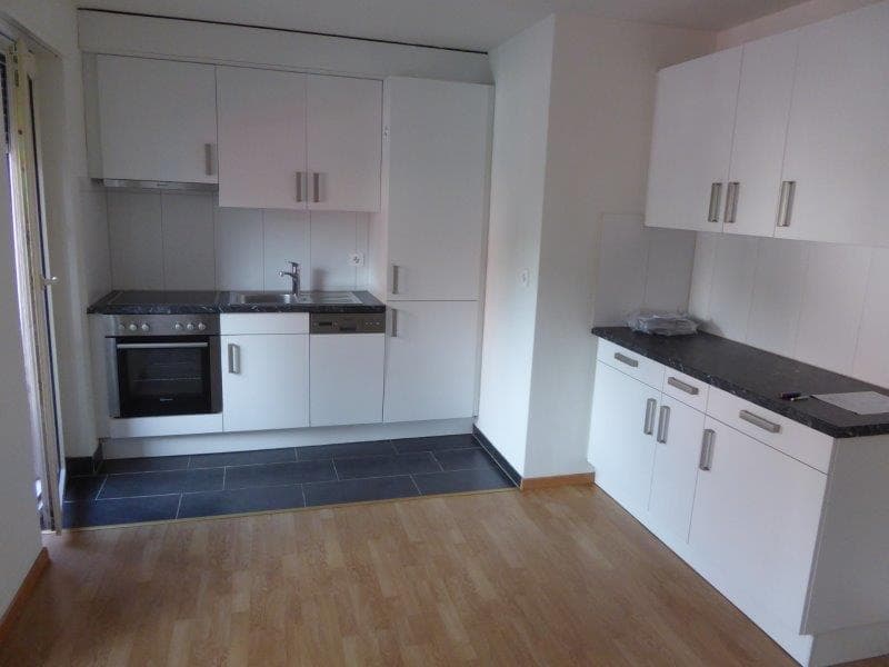 Spacious kitchen with white cabinets, black countertops, gas stove, and dishwasher. Hardwood flooring and tiled floor in the kitchen area.