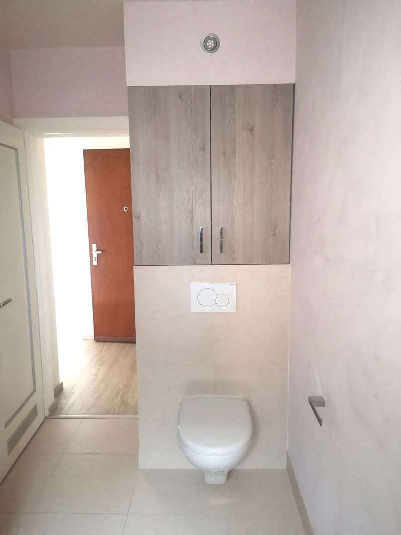 modern bathroom with white floor, white toilet, white walls, light wooden flooring in room behind