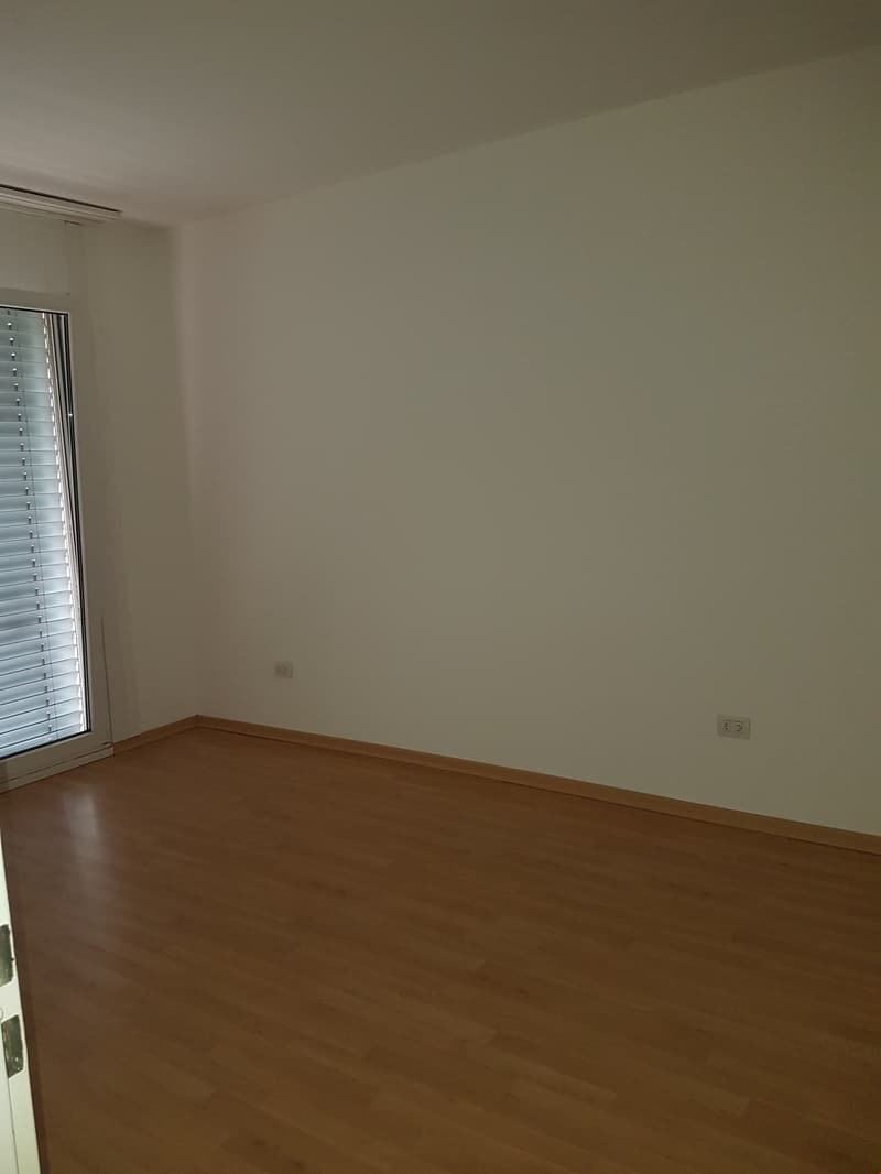 Empty room with white walls, wooden floor, sliding glass door leading to a balcony.
