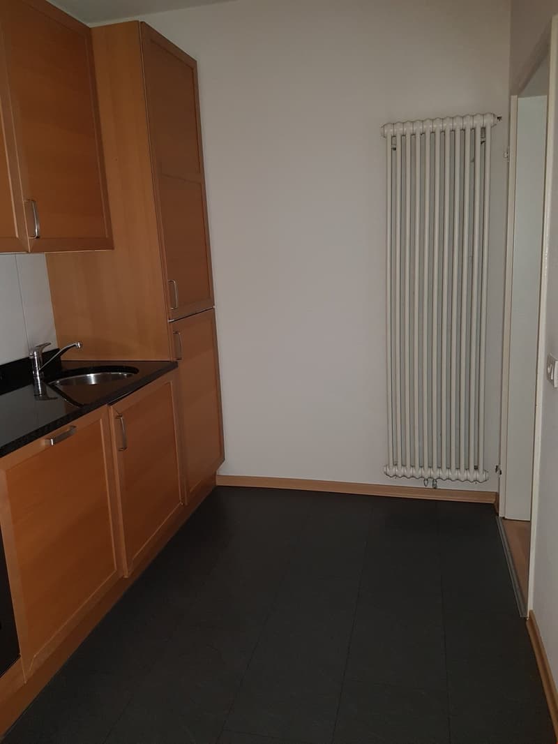kitchen with wooden cabinets, black countertop, stainless steel sink, and a white radiator