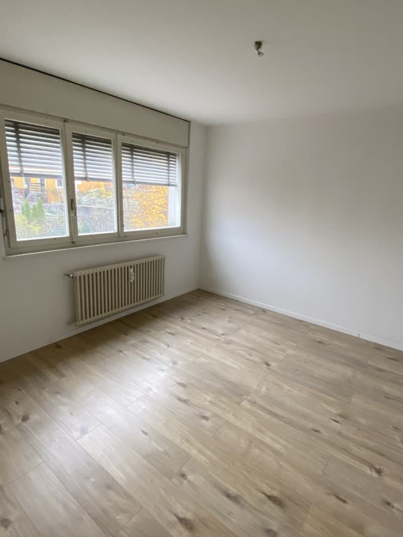 Spacious bedroom with large windows, hardwood flooring, and white walls.