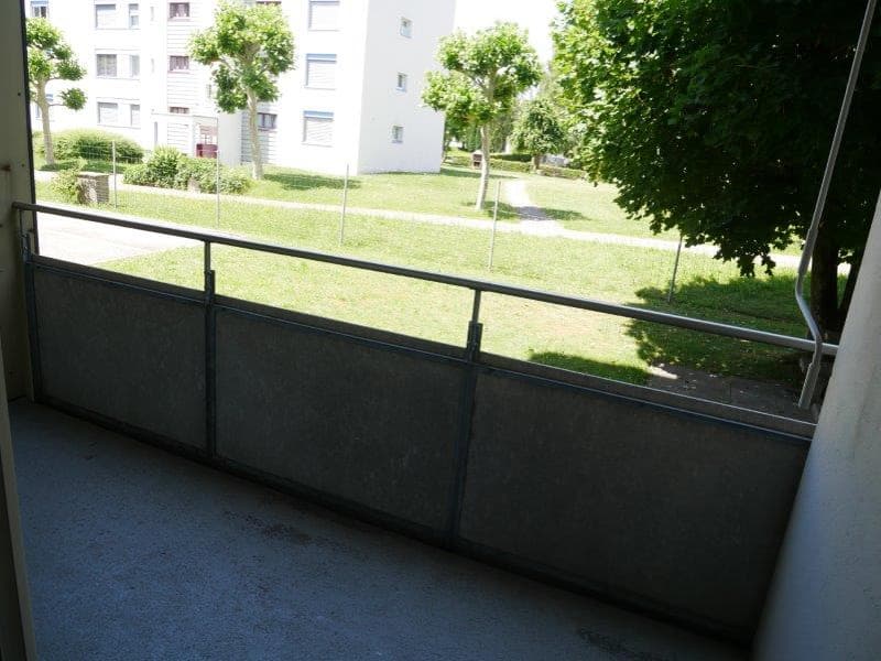 Metal railings, concrete wall, empty room, grass, shrubs, sidewalk, building in the background