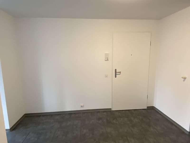 Empty room with white walls and gray flooring, with an entrance door