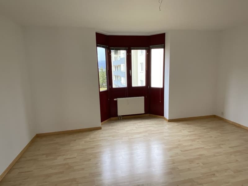 Empty room with wooden floor, three windows, radiator, and no furniture