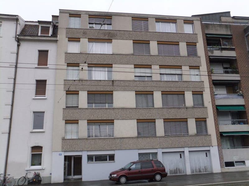 multi-story building, 6 floors, garage doors, balcony on 3rd floor, parked car in front