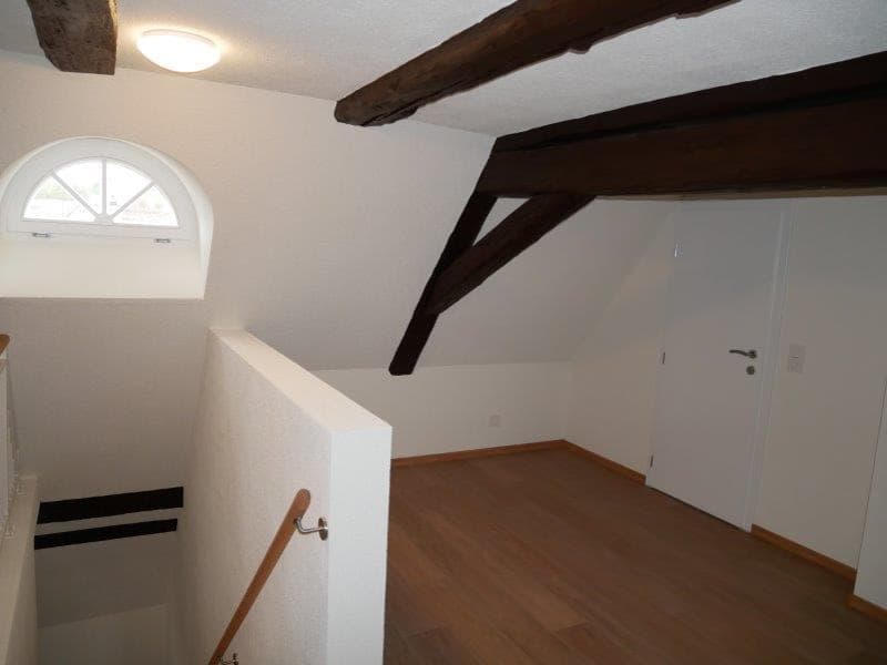 An empty room with wooden ceiling beams and walls, a window at the top of the stairs, wooden flooring, white walls, and a door.