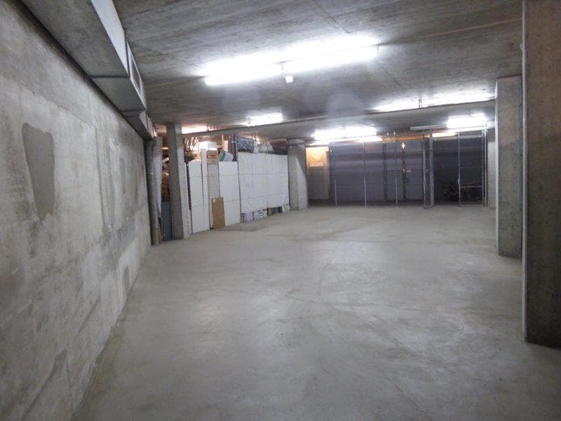 Underground parking space with white and gray walls, fluorescent lights on the ceiling, and storage boxes near the wall.