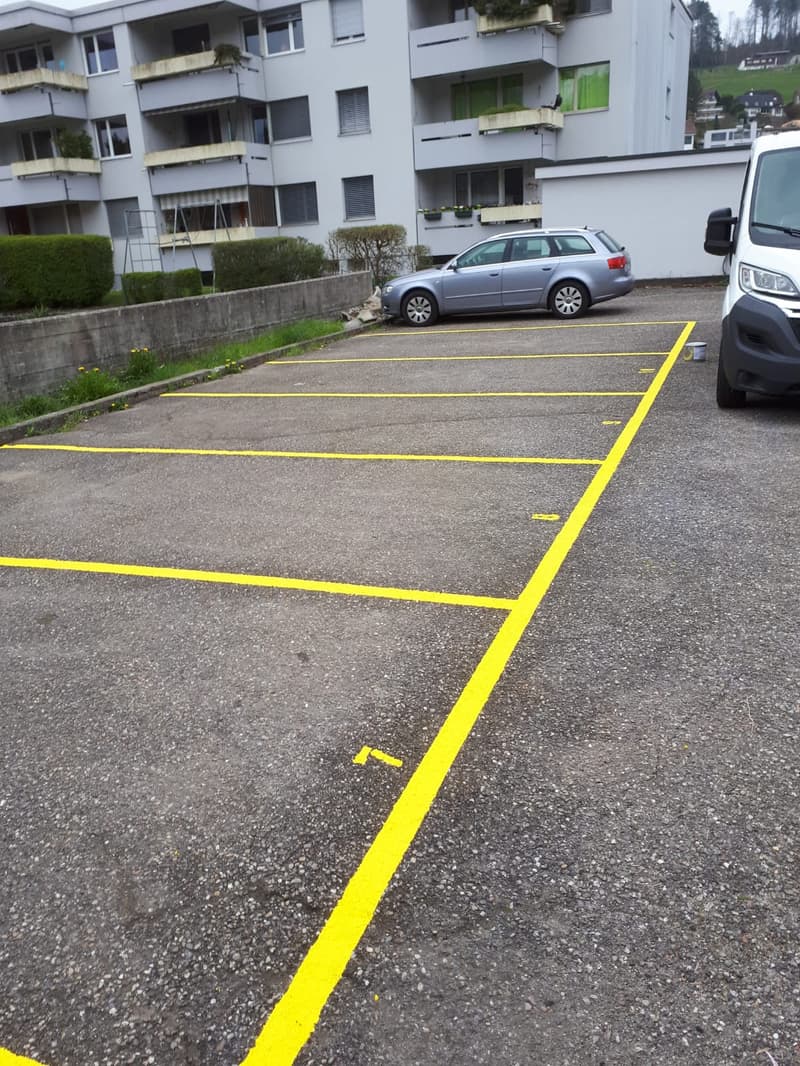 Large concrete parking lot with yellow parking spaces marked, building in the background, parked cars