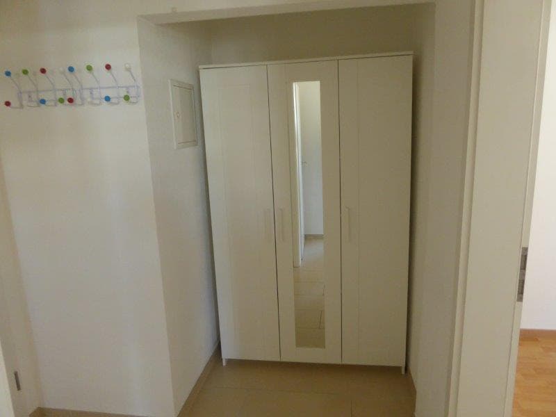 Empty room with white wardrobe with mirror, tiled floor, hooks on the wall