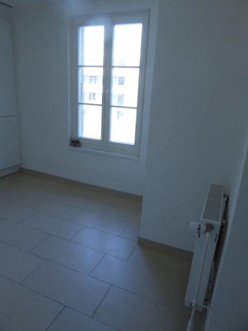 empty room with white walls, white tiled floor, a window, a radiator