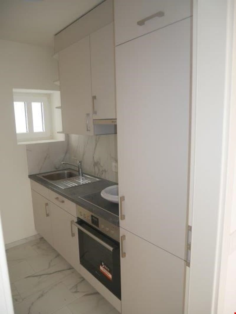 modern kitchen with white cabinets, marble countertop, stainless steel sink, oven, dishwasher, and a window