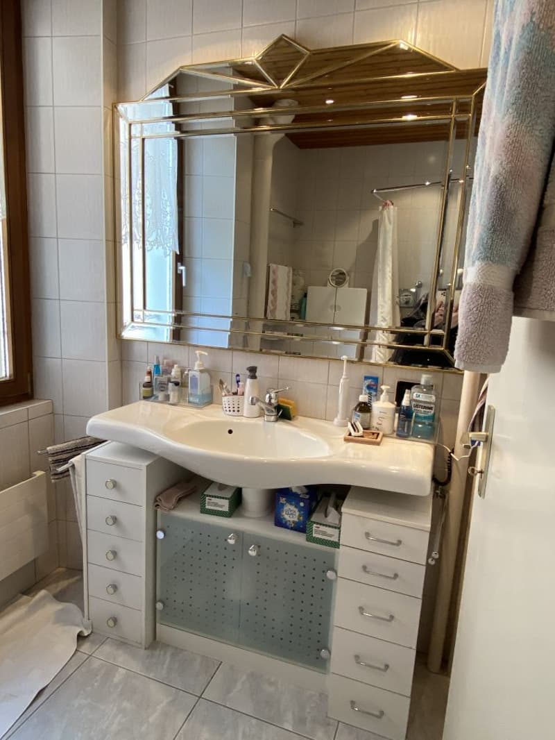 Bathroom with white tiles, large mirror, white sink, white cabinets, shower curtain, towels, toiletries