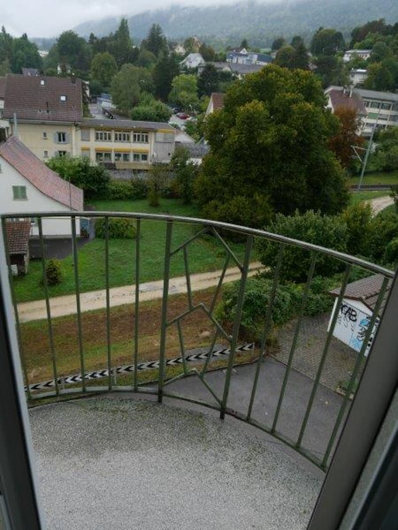 Balcony with metal railing, view of a grassy area and houses
