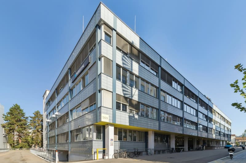 modern office building with multiple floors, large windows, parking lot, bicycles parked, signboard with text 'PUREGYMN'
