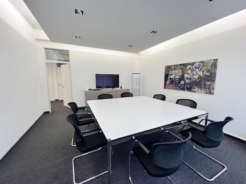 white table, black chairs, flat screen TV, white walls, gray carpet