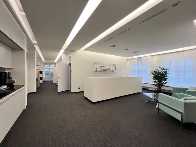 modern office space with white walls, black flooring, white reception desk, white cabinets, white couch, glass table, plant, and windows with white curtains