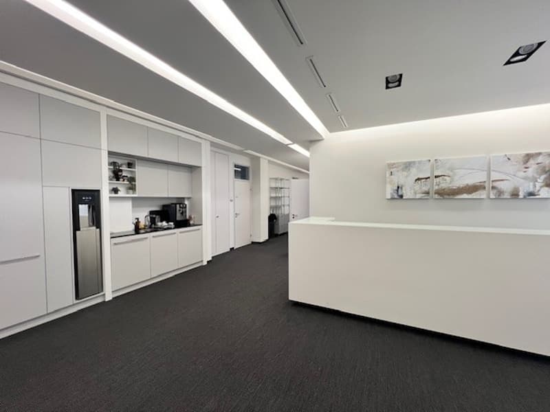 modern office room, white walls, white cabinets, black carpet, white reception desk, modern lighting, kitchen area with coffee machine, microwave, refrigerator