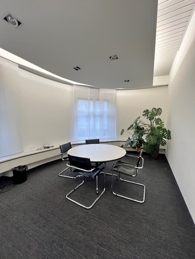 empty meeting room with a round table, 5 chairs, a plant, and a window
