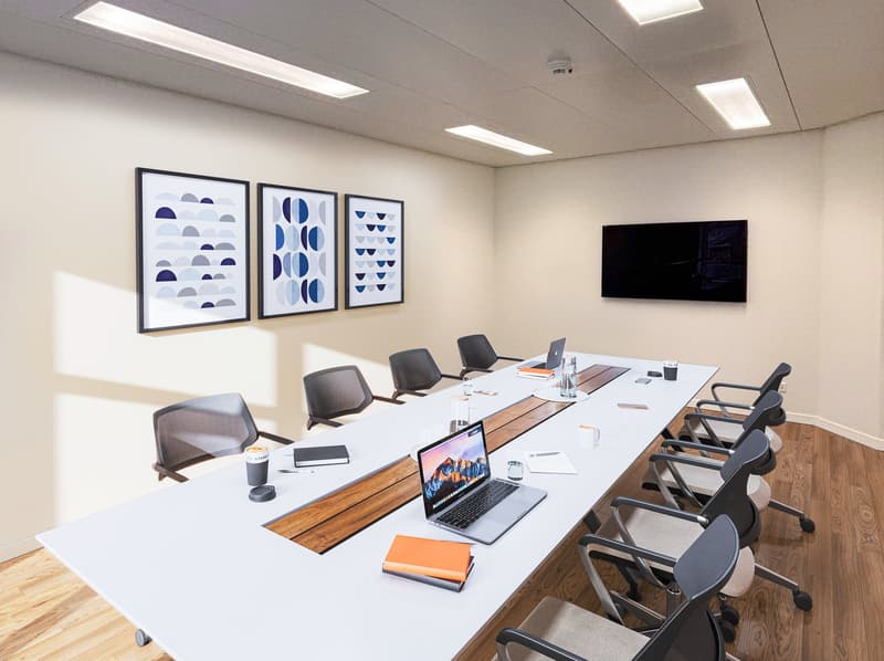 A conference room with a long table, chairs, laptops, books, and a TV mounted on the wall.