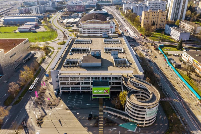 Aerial view of a large building with a parking lot, surrounded by roads and other buildings.