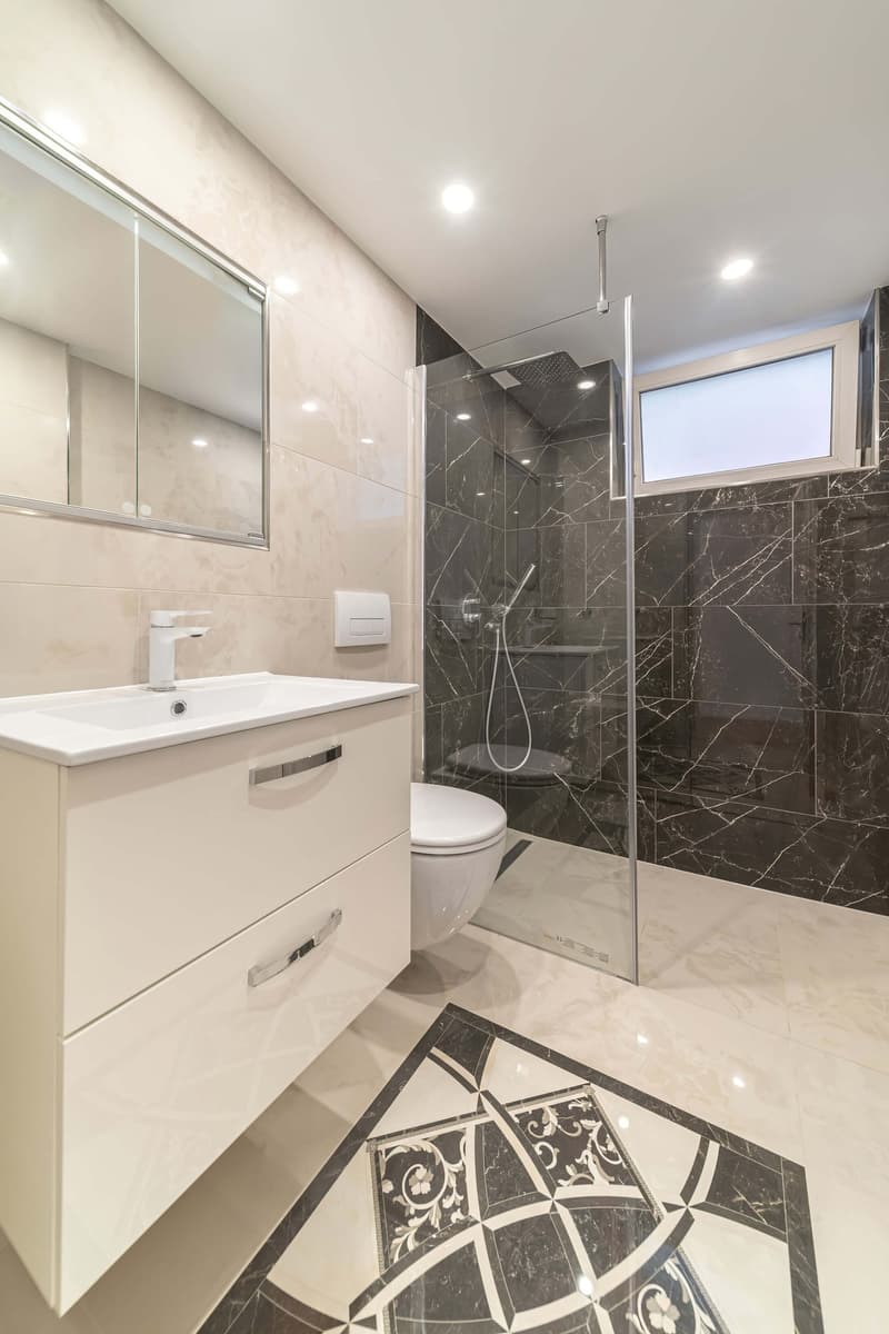 modern bathroom with white vanity, marble tiles, glass shower, toilet, sink with faucet, mirror