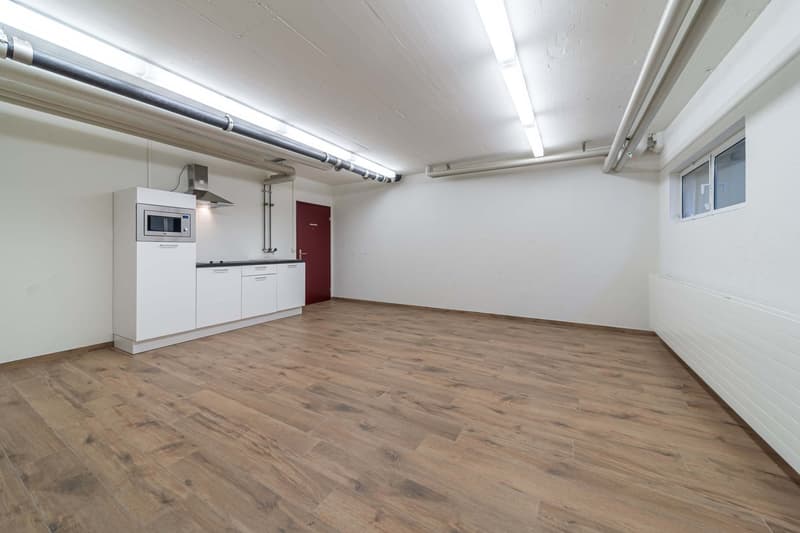 Open-plan studio apartment with hardwood-style flooring, white walls, and a kitchenette with a microwave and dishwasher.