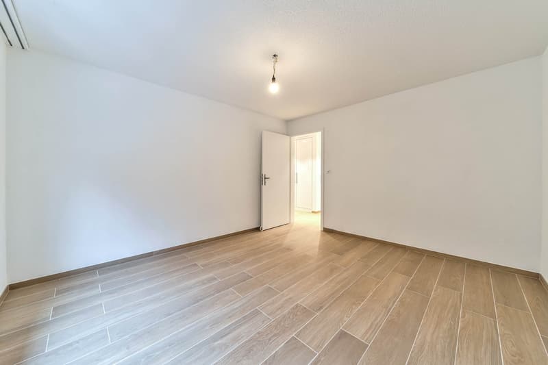 Empty room with wooden floors, white walls, and a single pendant light