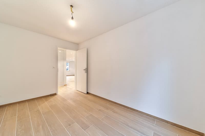Empty room with wooden floors and white walls, open door leading to another room