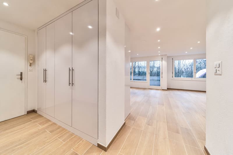 Empty hallway with wooden floors, large wardrobes, two windows on the end