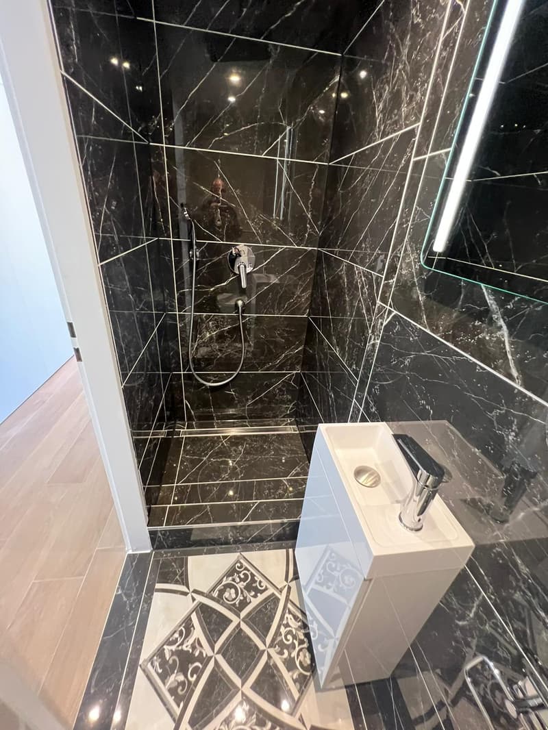 modern bathroom with black marble tiles, walk-in shower with integrated shower head, sink, mirror, and wooden floor