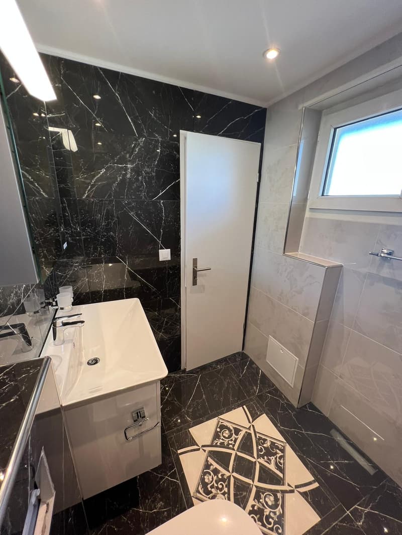 modern bathroom with marble tiles, white vanity, glass shower door, white toilet