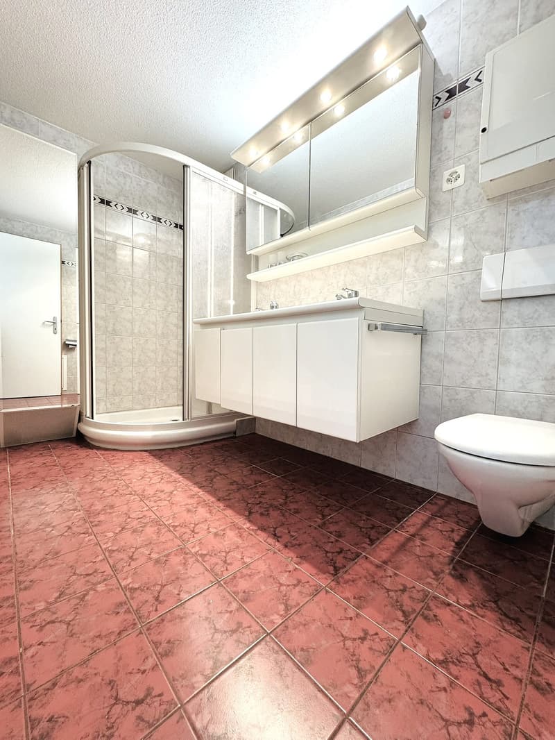 Bathroom with a shower stall, mirror, sink, and toilet. The walls and floor are tiled.