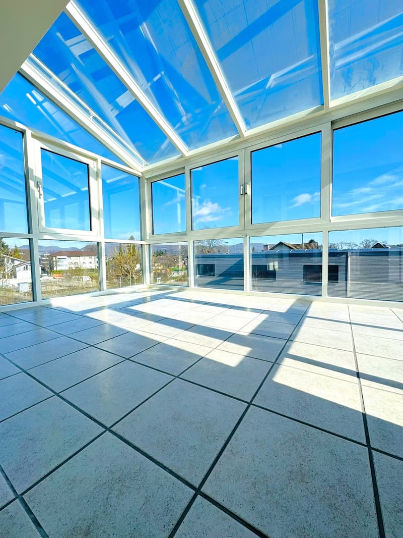 An empty room with a glass ceiling and walls, tiled floor, and a view of the outside.