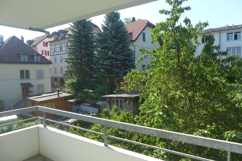 Balcony with metal railing, overlooking a garden with trees and a small house