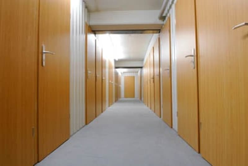 Long, narrow hallway with wooden doors on both sides and a grey floor.