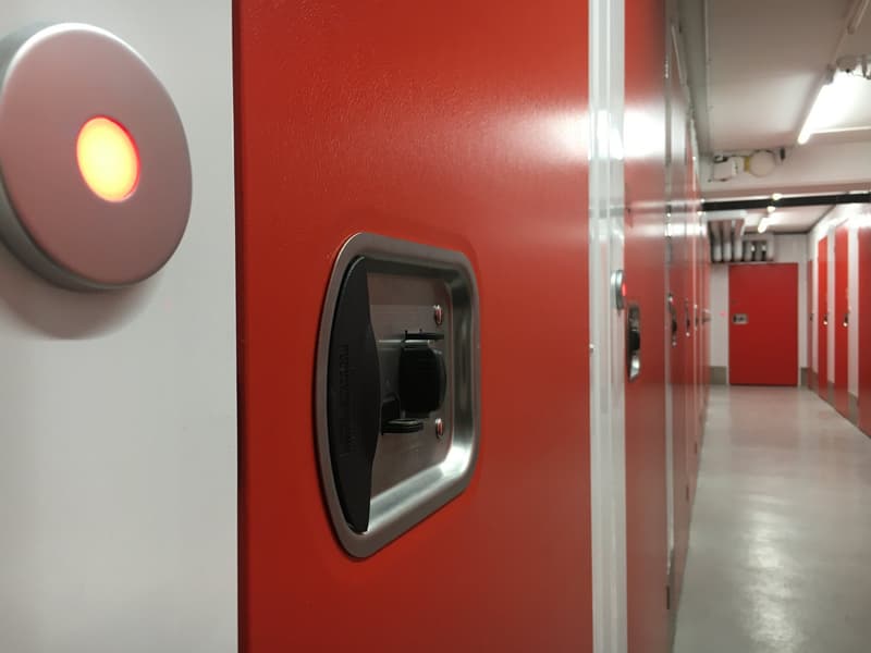 The image shows a hallway with a red wall and a security camera or intercom system mounted on the wall. The hallway appears to have multiple doors leading to other rooms or units.