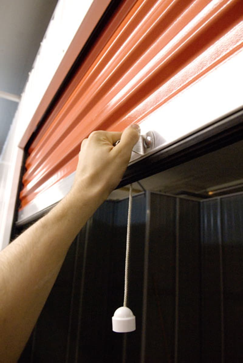 The image shows a hand pulling open an orange curtain or blind, revealing a dark interior space behind it.