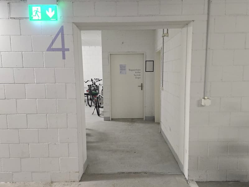 White brick walls, green emergency exit sign, bicycles parked, white door, number 4 on the wall