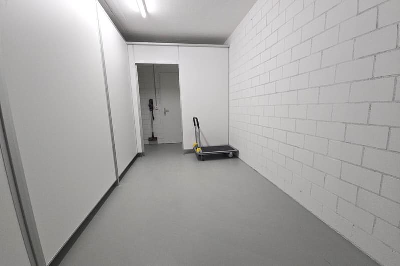 Empty room with white brick walls, gray floor, hallway leading to a room with a door.