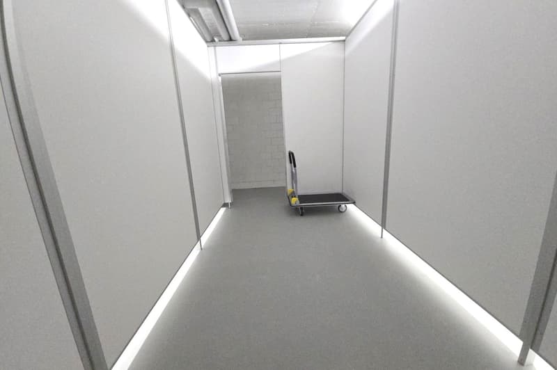 white walls, gray floor, white light strips along the walls, a cart at the end