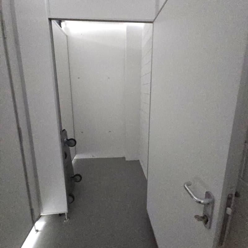 Storage room, white walls, gray flooring, door on left with shelving, door on right